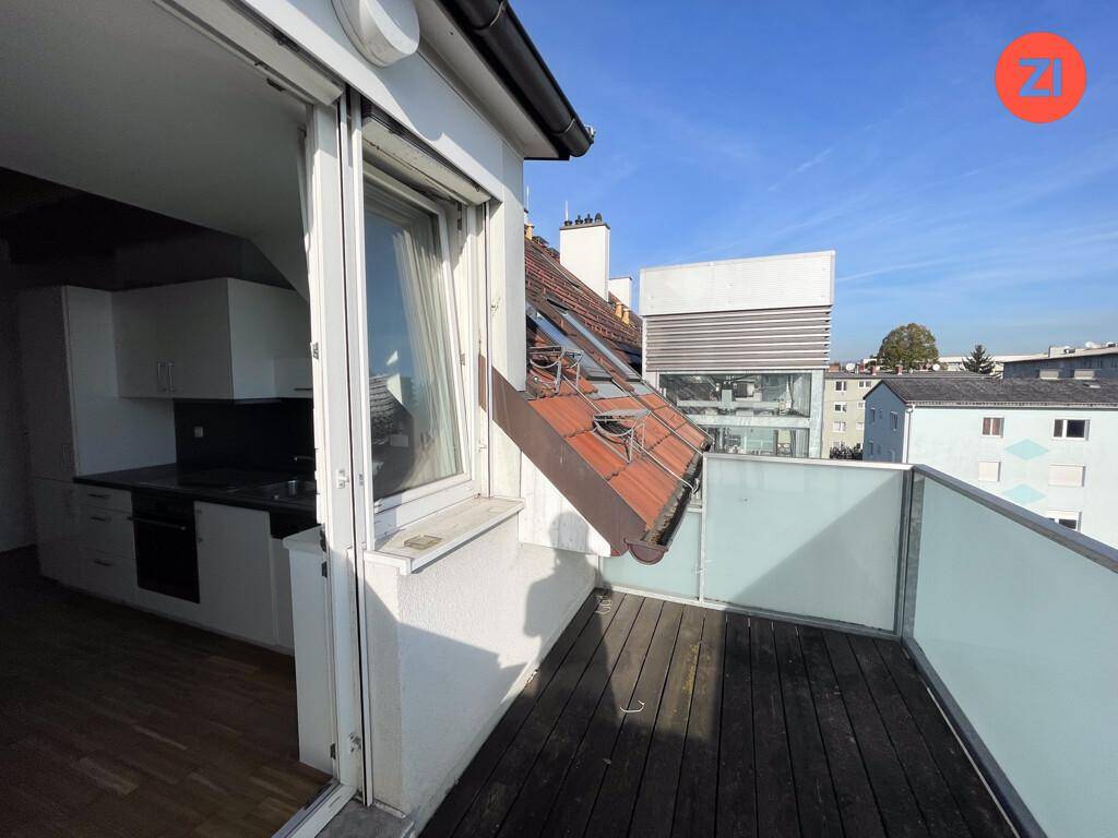 Sonniger Balkon mit Holzboden und Glasgeländer, bietet Blick auf die umliegenden Gebäude.