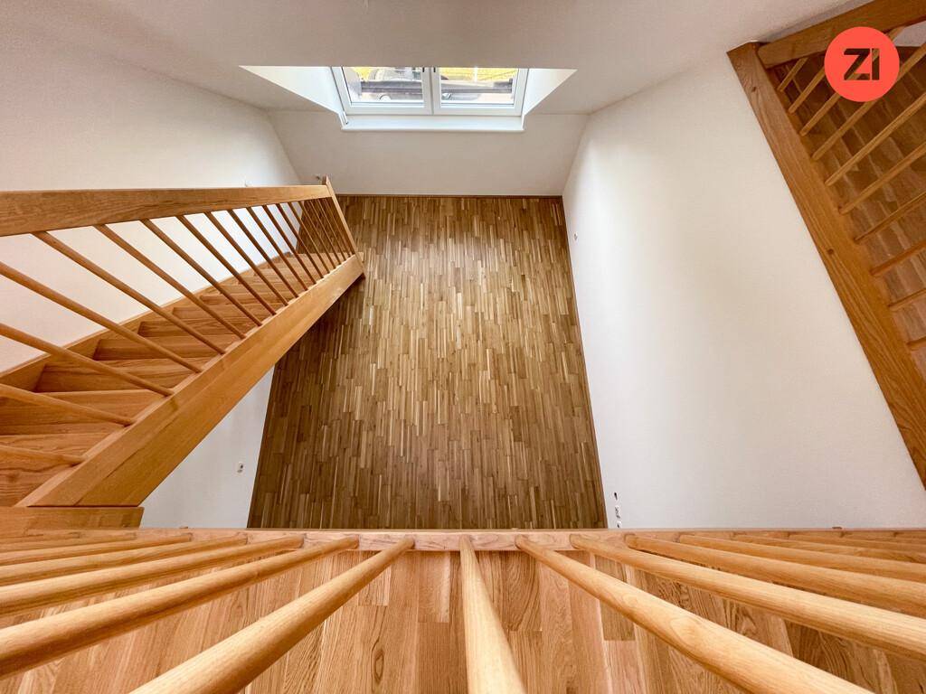 Blick von oben auf eine Holztreppe mit Parkettboden und einem Dachfenster, das den Bereich erhellt.