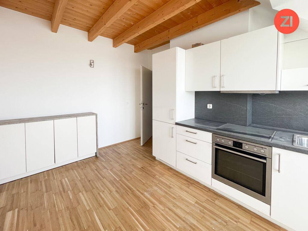 Heller Küchenbereich mit weißen Einbauschränken, Holzbalken und Parkettboden in der Dachgeschosswohnung.