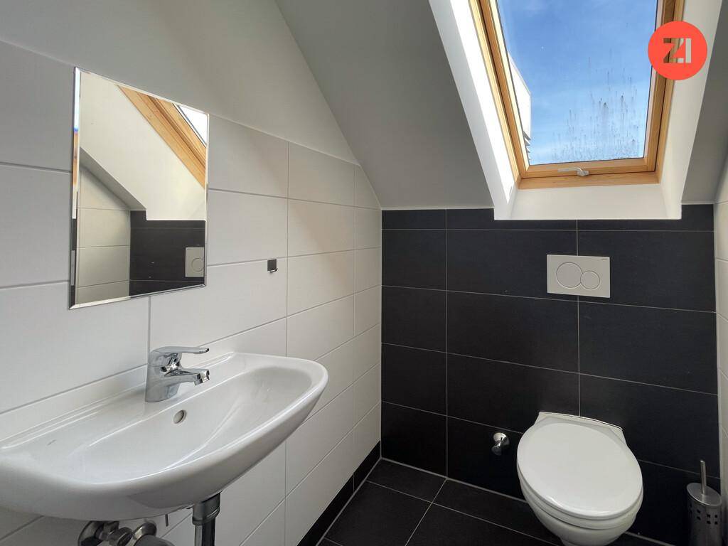 Separates WC mit Toilette, Waschbecken, Spiegel und Dachfenster, modern gefliest.