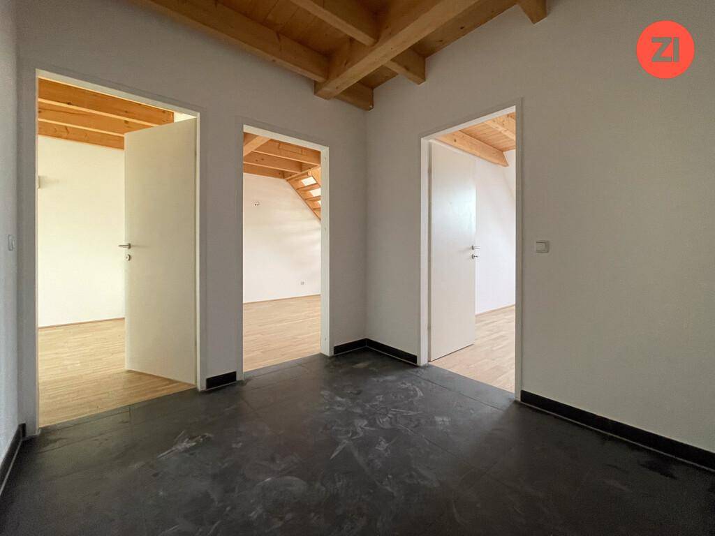 Leerer Raum mit dunklem Boden und mehreren offenen Türen zu weiteren Zimmern mit Holzbalken.