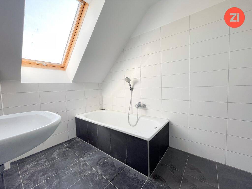 Modernes Badezimmer mit Badewanne, Waschbecken, Fliesen und einem Dachfenster im Dachgeschoss.