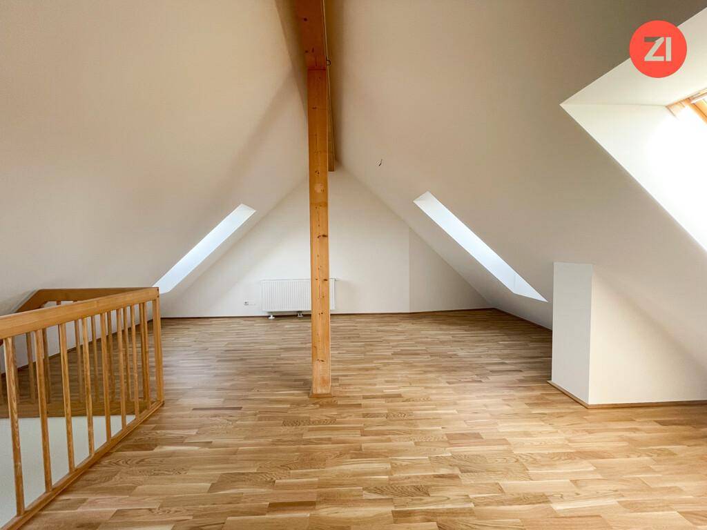 Geräumiger Dachbodenraum mit Holzboden, sichtbaren Balken und mehreren Dachfenstern für viel Licht.