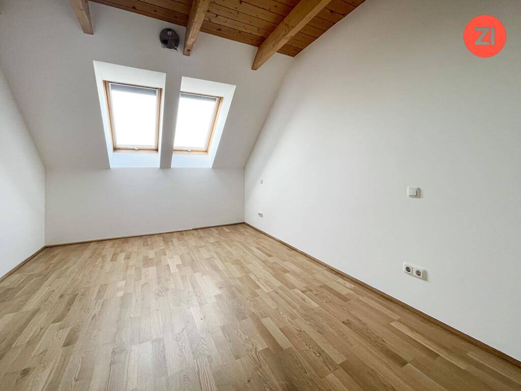 Helles Schlafzimmer im Dachgeschoss mit Parkettboden, weißen Wänden und zwei Dachfenstern.
