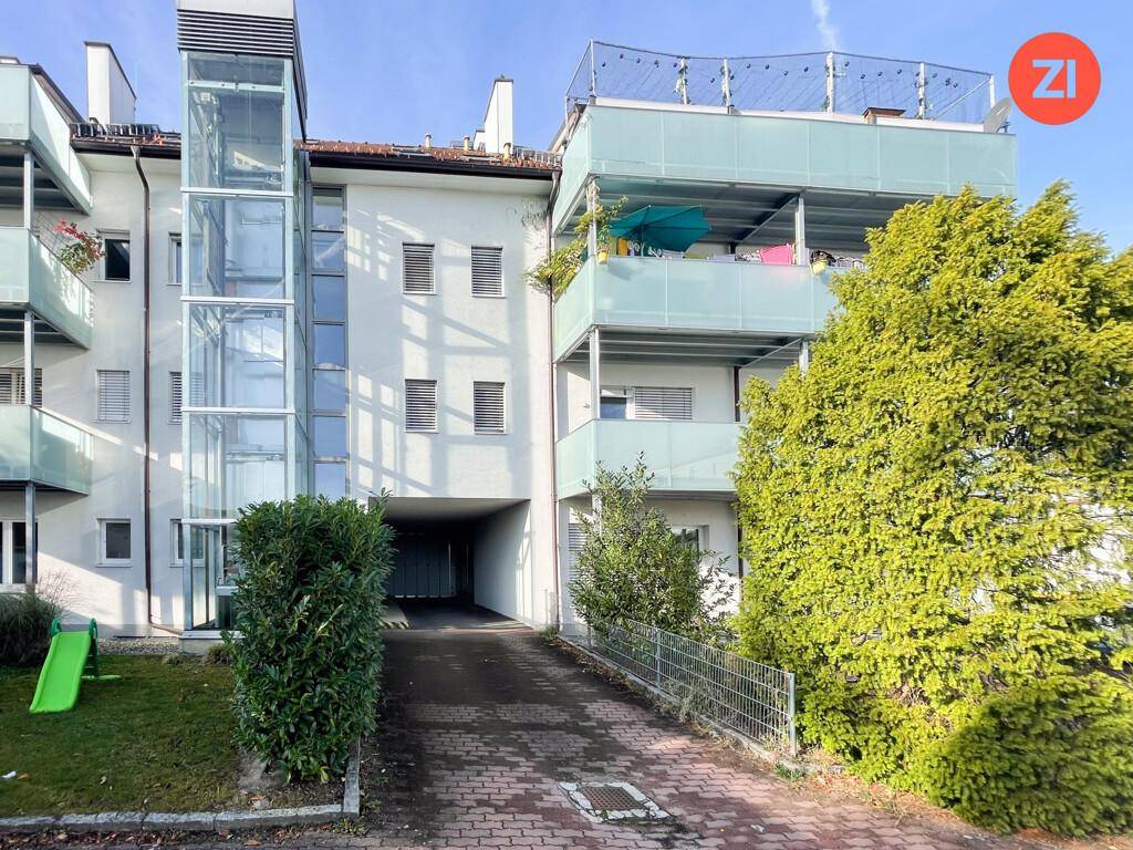 Modernes Mehrfamilienhaus mit Balkonen, externem Glasaufzug und gepflegter Außenanlage.