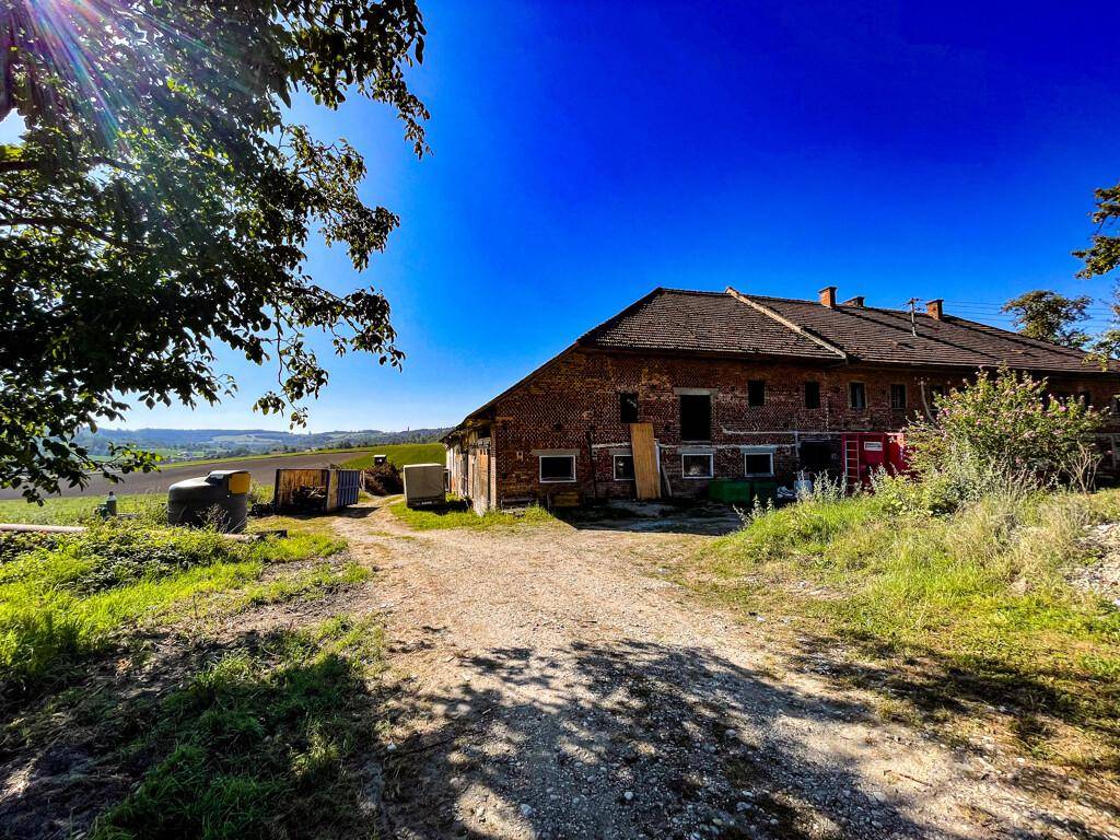 Weitläufige Ansicht des Hauptgebäudes mit Ziegelfassade und umliegenden Feldern unter blauem Himmel.