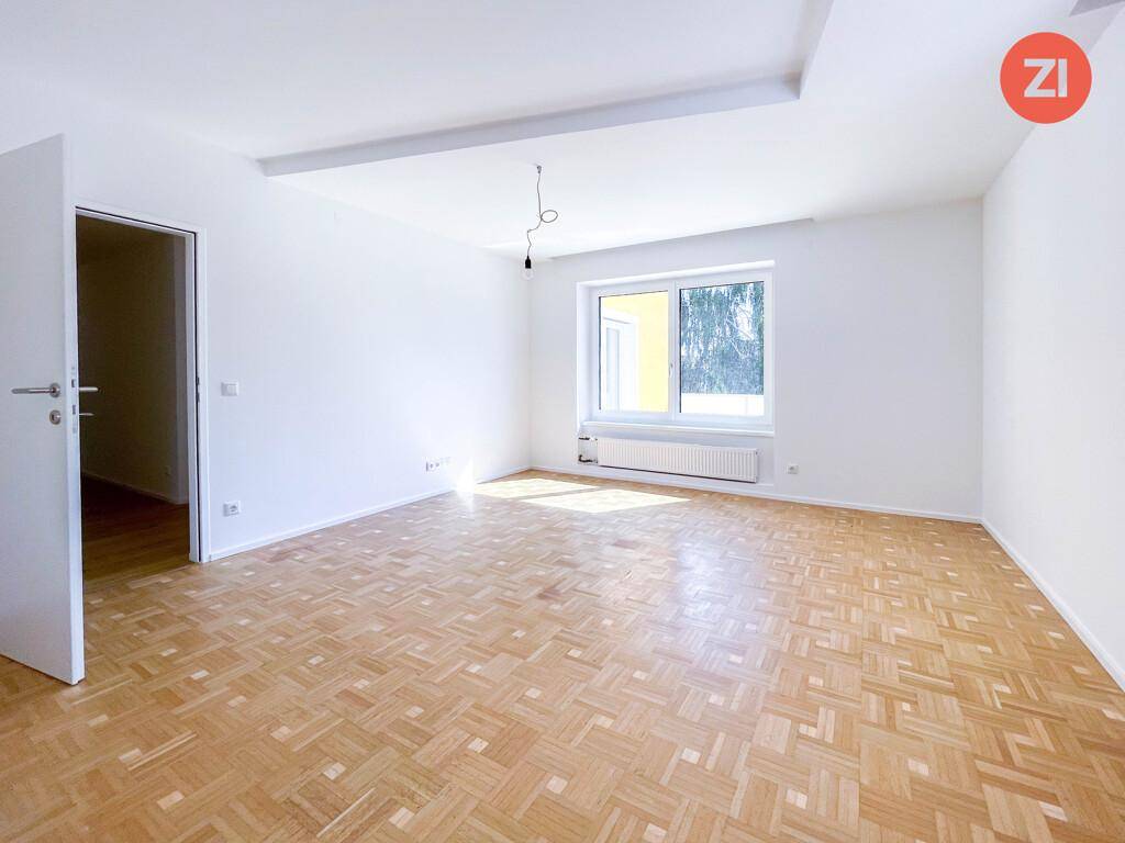 Geräumiger, heller Raum mit Parkettboden und einem Fenster, das den Blick nach draußen freigibt.