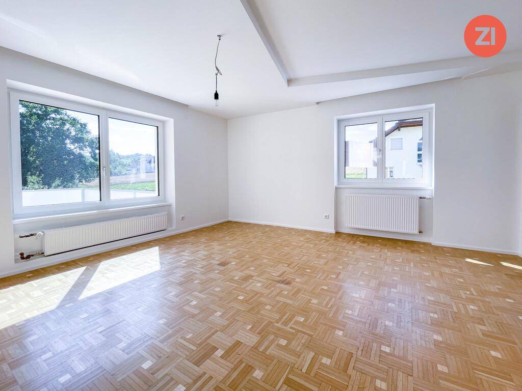 Heller Wohnraum mit Parkettboden und großen Fenstern, die viel Tageslicht hereinlassen.