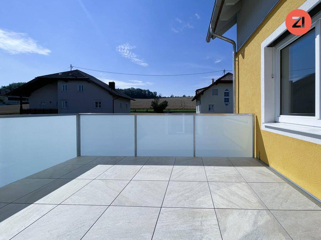 Große, geflieste Terrasse mit moderner Glasbrüstung und Blick auf die ländliche Umgebung.