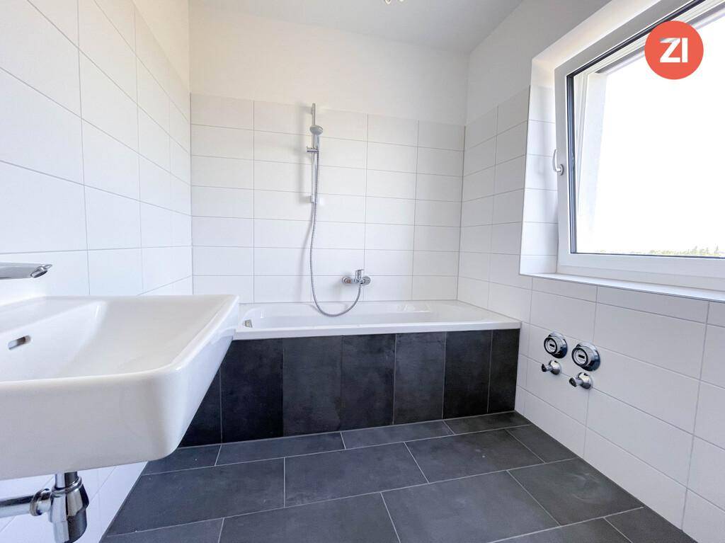 Modernes Badezimmer mit Badewanne, Waschbecken und weißen sowie dunklen Fliesen.
