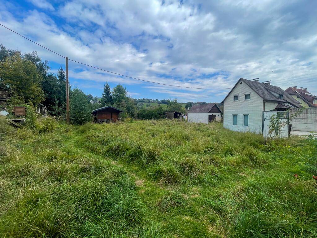 Weitläufiges, grasbewachsenes Grundstück mit einem kleinen Schuppen und einem Wohnhaus im Hintergrund.