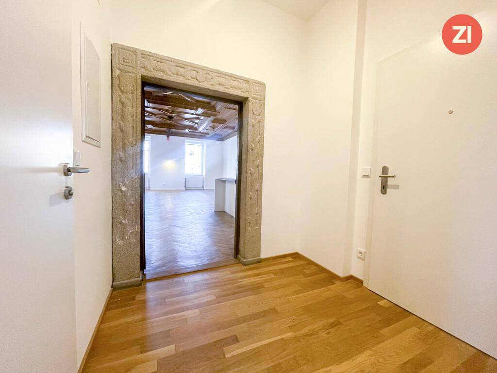 Eingangsbereich mit Holzboden und einem kunstvoll verzierten Steinportal, das in den Wohnbereich führt.