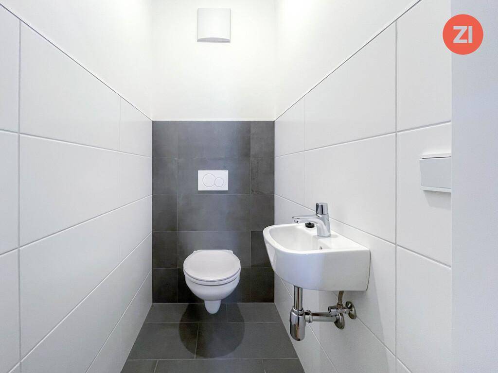 Separates Gäste-WC mit wandhängender Toilette, kleinem Waschbecken und modernen Fliesen in Weiß und Grau.