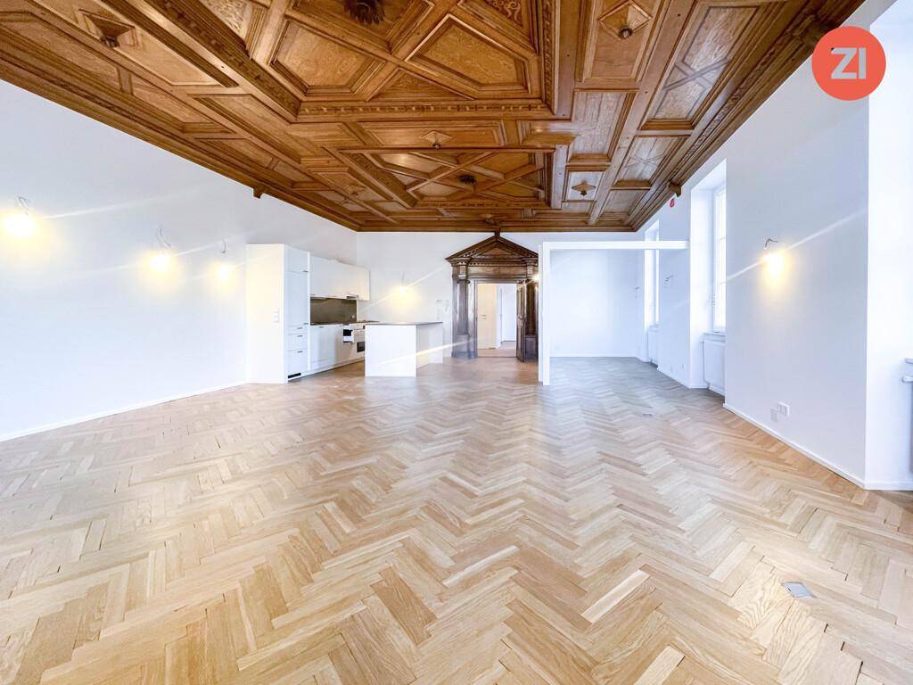 Weitläufiger Wohnbereich mit eleganter Holzkassettendecke und klassischem Fischgrätparkett, ideal für offenes Wohnen.