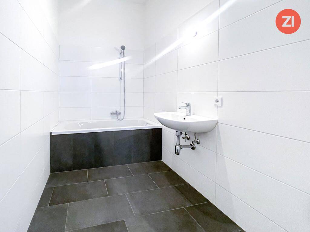 Modernes Badezimmer mit weißen Wandfliesen, dunklem Boden und einer Badewanne mit Duschfunktion.