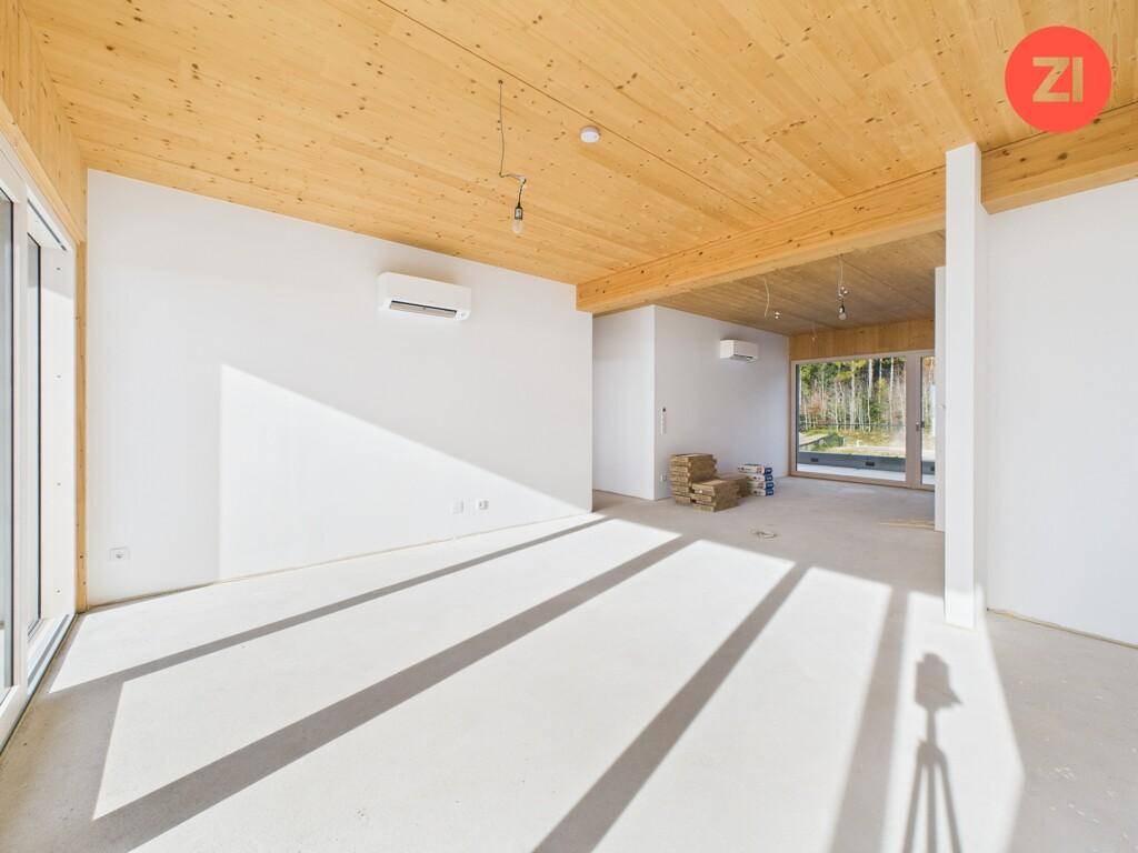 Geräumiger Rohbau mit sichtbarer Holzdecke und großen Fensterfronten für viel Tageslicht.