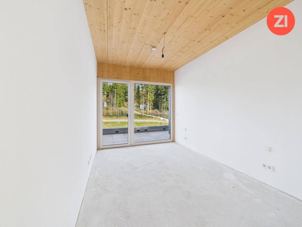 Heller Rohbau mit Holzdecke, Betonboden und großen Fenstern mit Blick ins Grüne.
