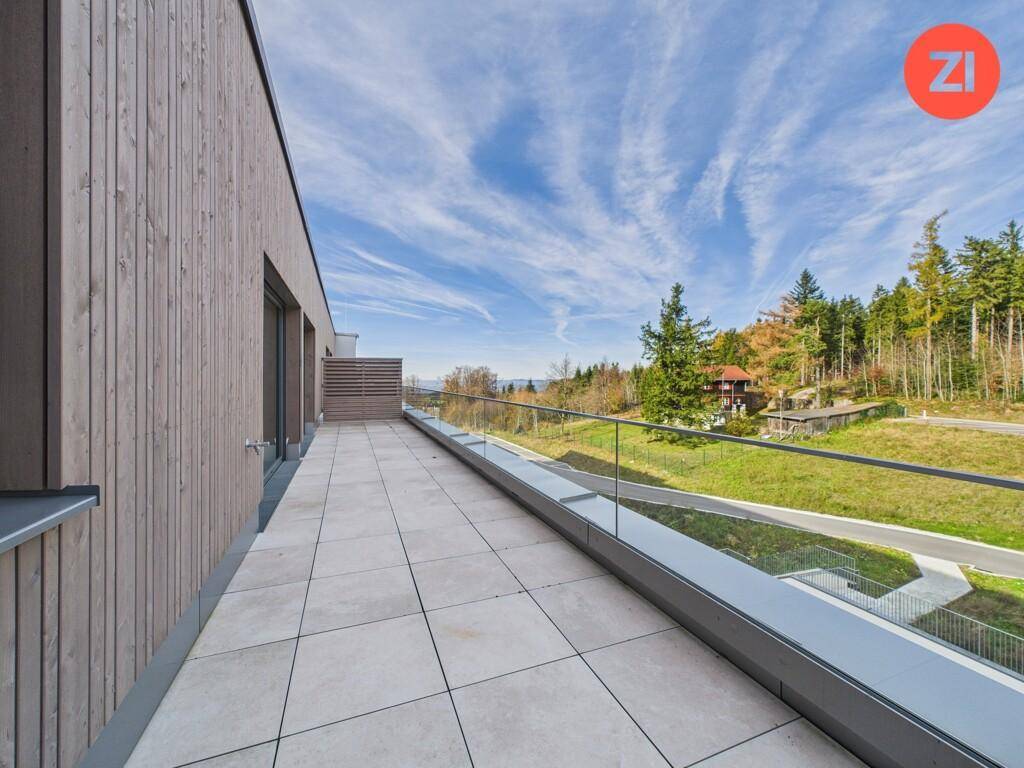 Geräumige Terrasse mit Holzwand, Fliesenboden und Blick auf die umliegende Natur und Bäume.