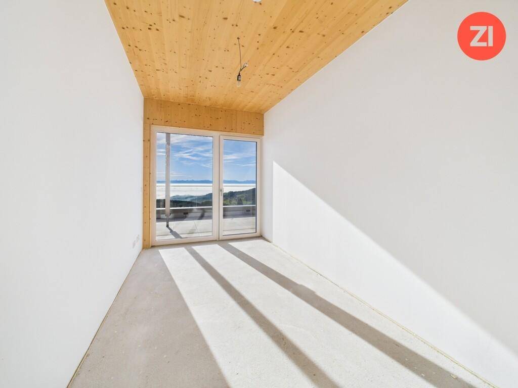 Unfertiger Raum mit Holzdecke und großen Fenstern, die einen weiten Blick über die Landschaft bieten.