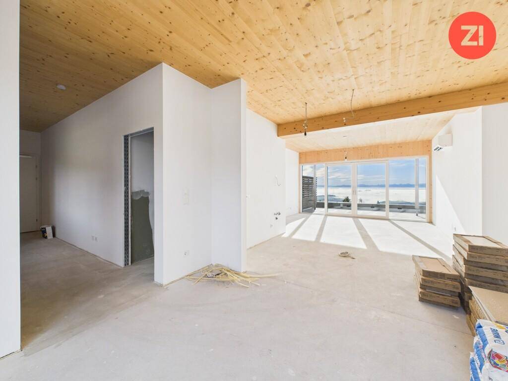 Unfertiger Innenraum mit Holzbalkendecke, Betonboden und großen Fenstern mit weitem Ausblick.