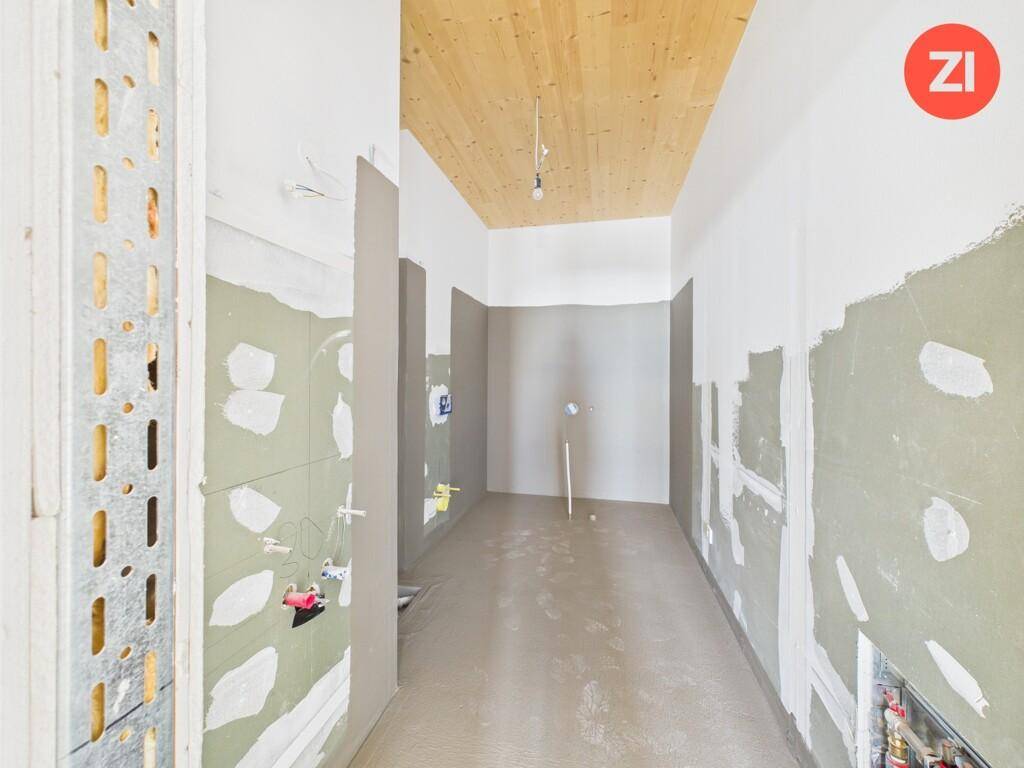Rohbau eines Badezimmers oder Hauswirtschaftsraums mit sichtbaren Installationen und Holzdecke.