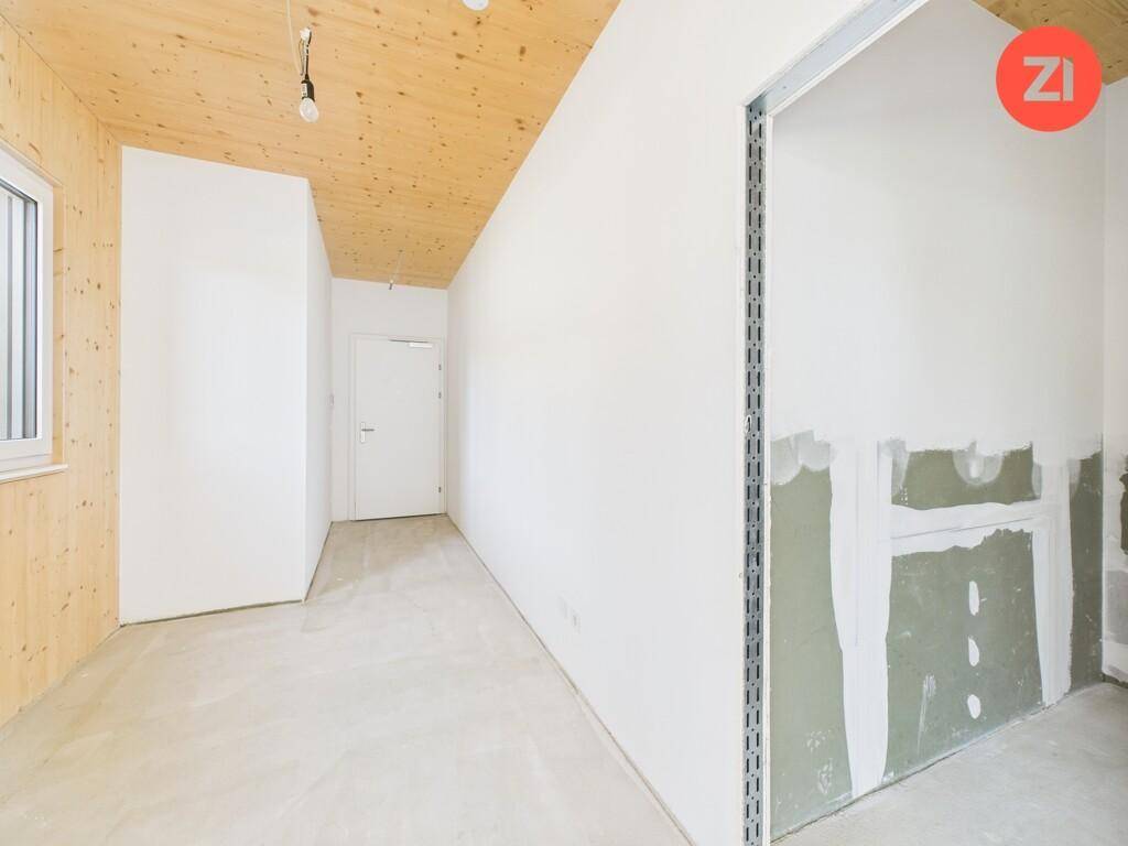 Flur im Rohbauzustand mit Holzdecke und unfertigen Wänden, führt zu weiteren Räumen.