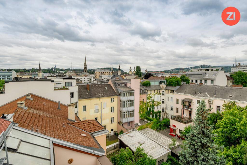 Panoramablick über die Dächer der Stadt mit grünen Bäumen und historischen Gebäuden.