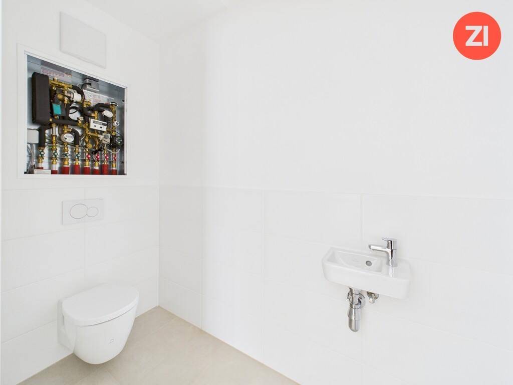 Funktionelles Gäste-WC mit weißen Fliesen, wandhängender Toilette und kleinem Waschbecken.