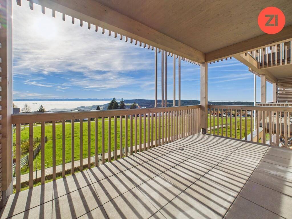 Großer sonniger Balkon mit Holzbalken, Fliesenboden und weitem Blick über die Landschaft.