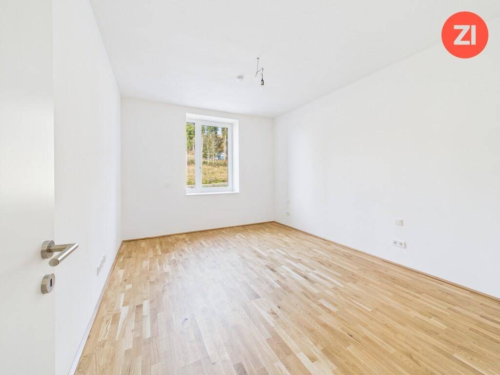 Ruhiges Zimmer mit Holzboden und einem großen Fenster, das viel Tageslicht hereinlässt.