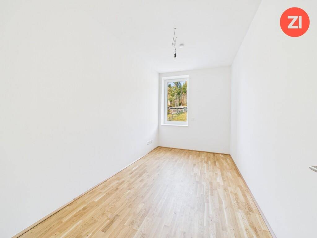 Gemütliches Zimmer mit Holzboden und einem Fenster, das einen Blick ins Grüne ermöglicht.