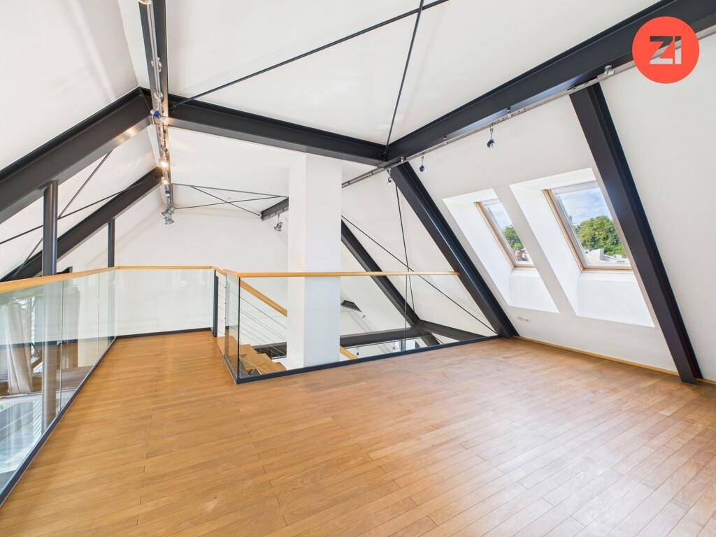 Offene Galerie im Dachgeschoss mit Holzboden, Dachfenstern und Glasgeländer.