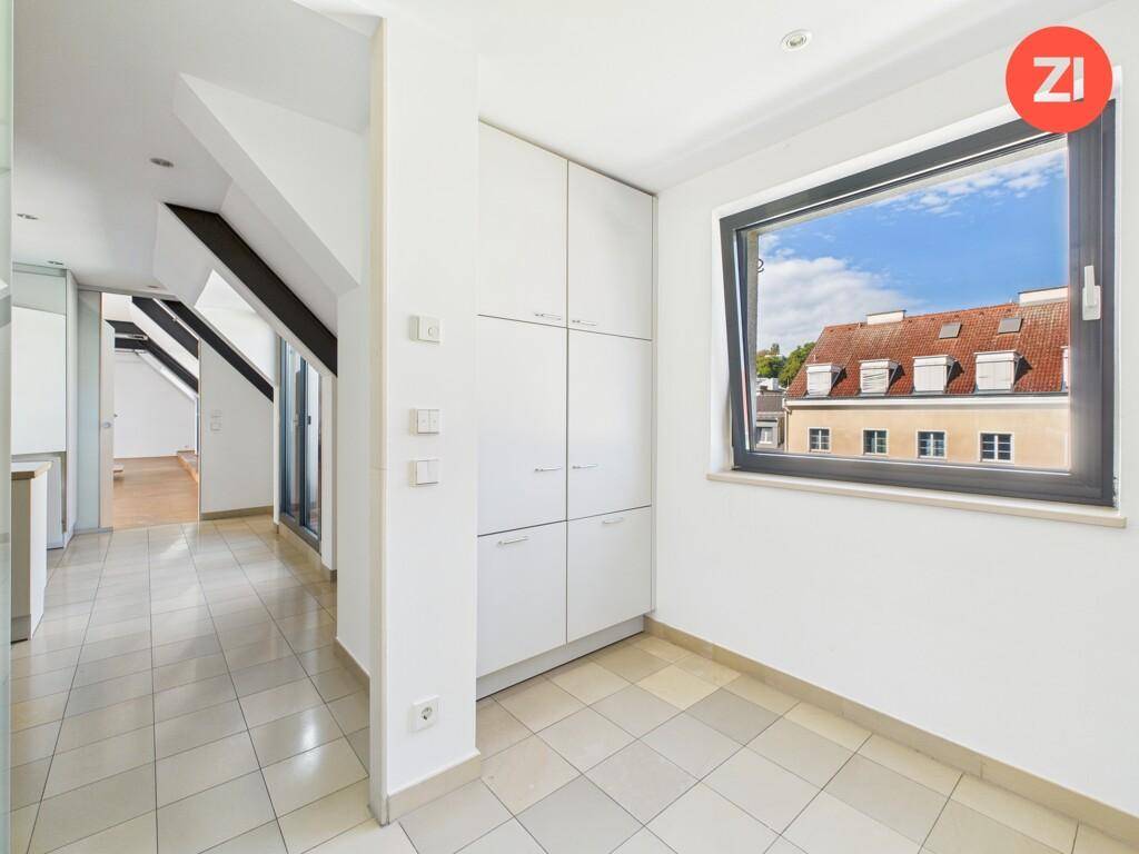 Heller Flur mit Fliesenboden, Einbauschränken und Fenster mit Blick auf Dächer.