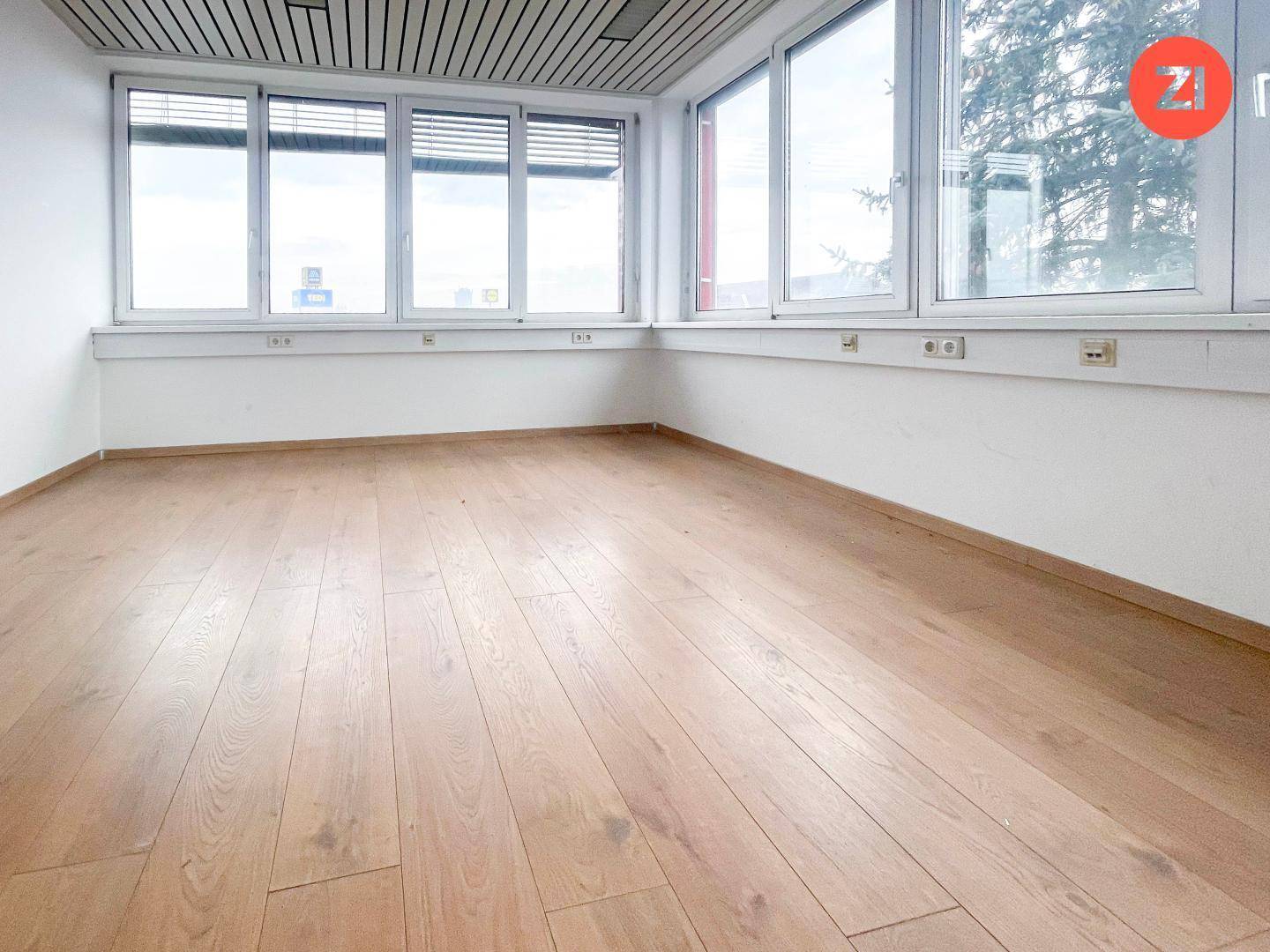 Geräumiges Büro mit viel Tageslicht durch die breite Fensterfront und hellem Laminatboden.