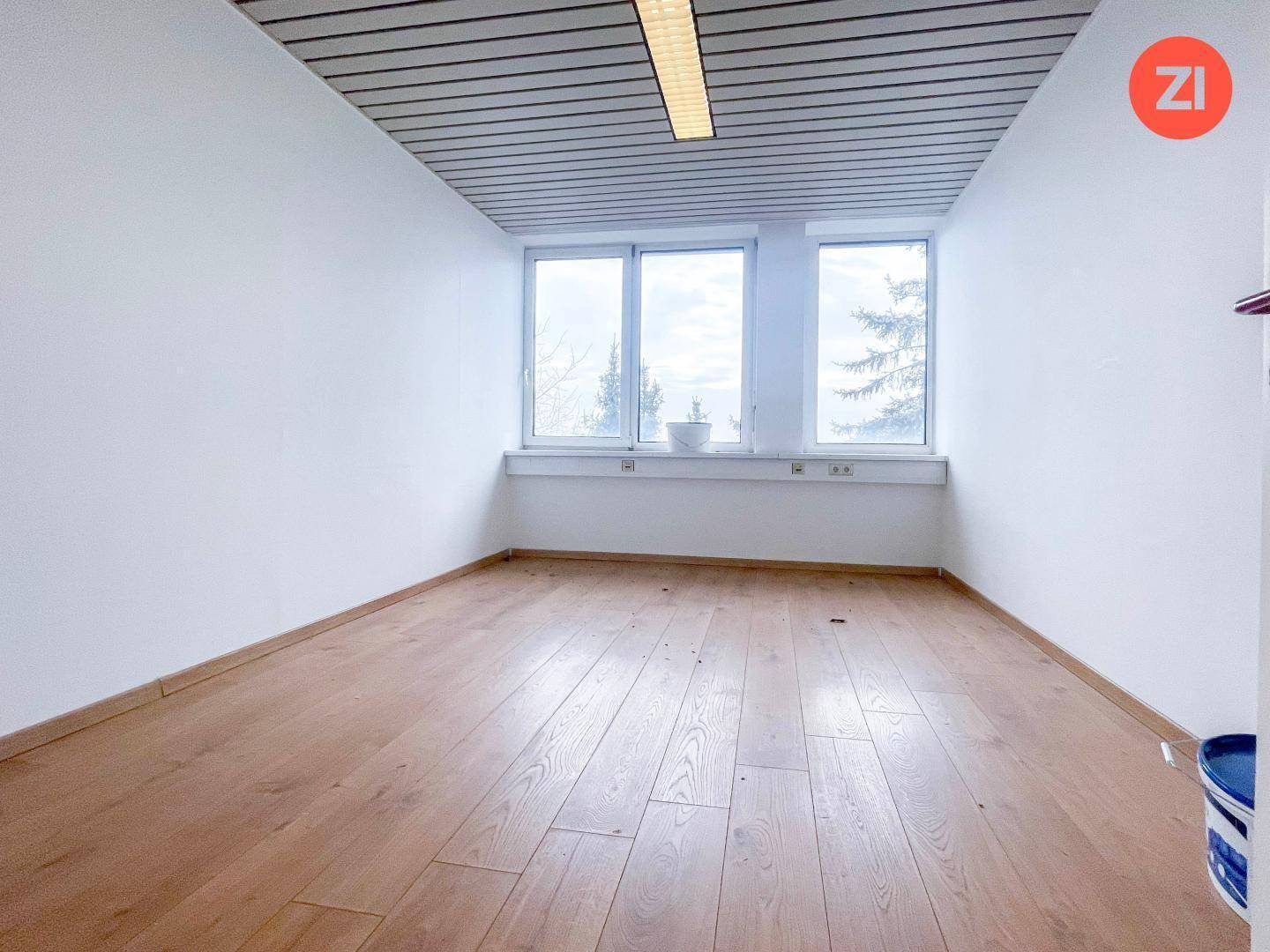 Kleineres, helles Büro mit zwei Fenstern, Laminatboden und einer abgehängten Decke.