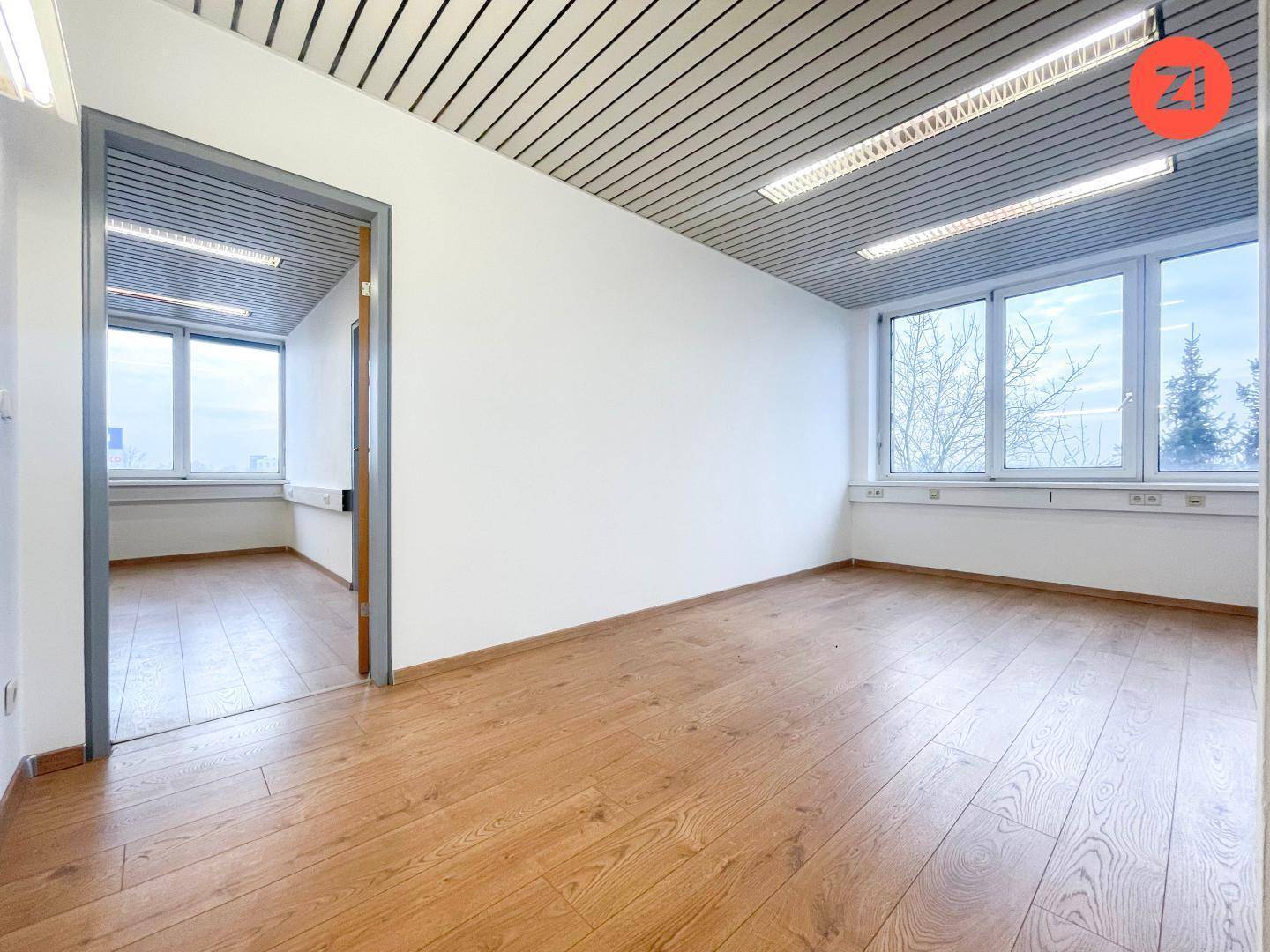 Helles Büro mit großen Fenstern und einer Tür, die den Zugang zu einem weiteren Raum ermöglicht.