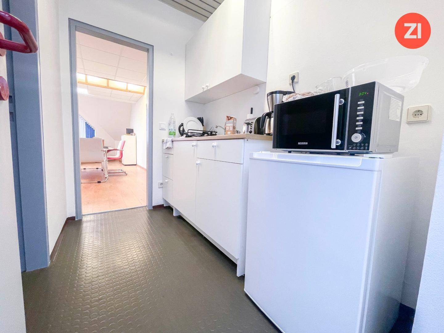 Kleine Küchenzeile mit weißen Schränken, Mikrowelle und Kühlschrank, ideal für Pausen.