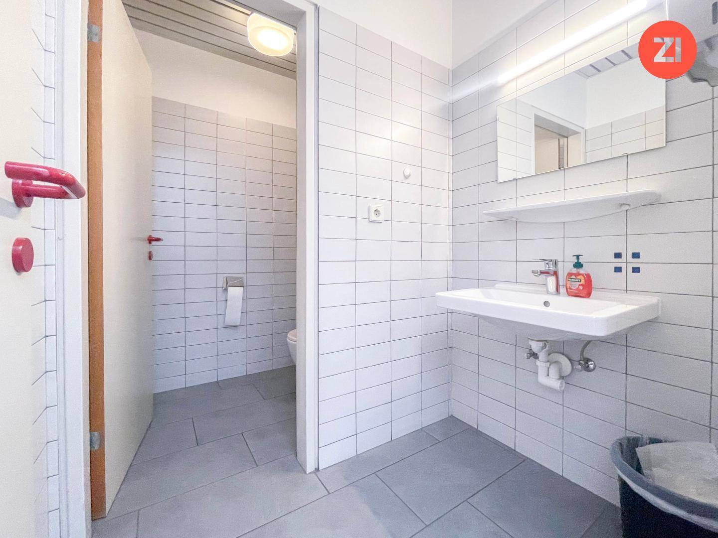 Modern gefliestes Badezimmer mit Waschbecken und Zugang zu einer separaten Toilettenkabine.