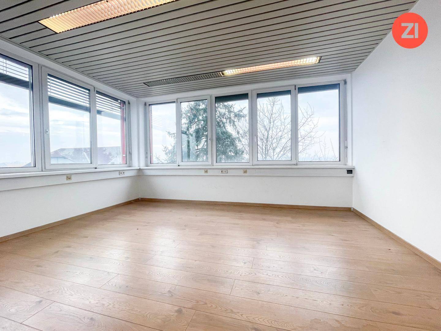 Eckbüro mit umfangreicher Fensterfront, die viel natürliches Licht hereinlässt, und Laminatboden.
