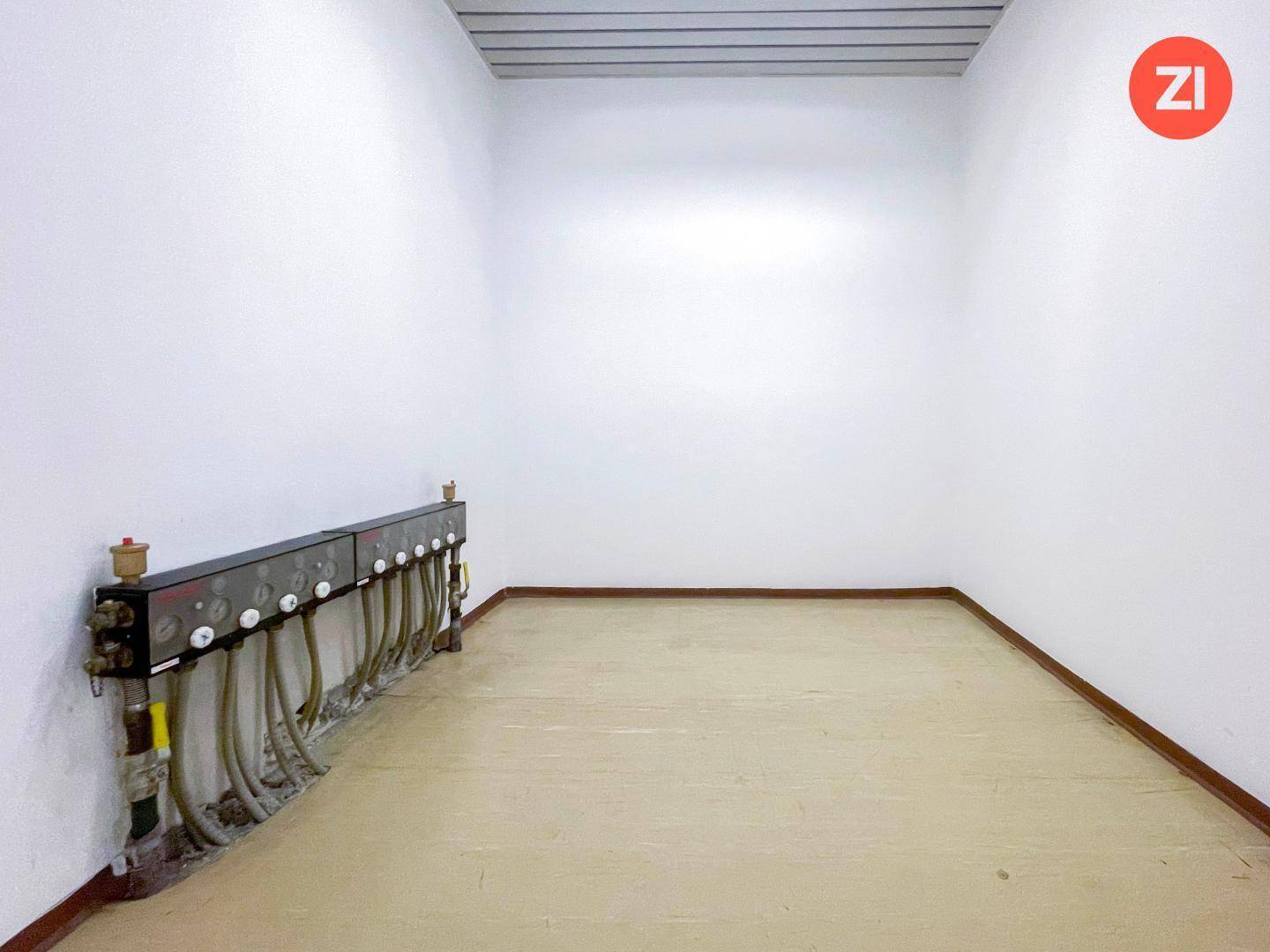 Technikraum mit sichtbaren Rohrleitungen und Anschlüssen entlang der Wand und hellem Boden.