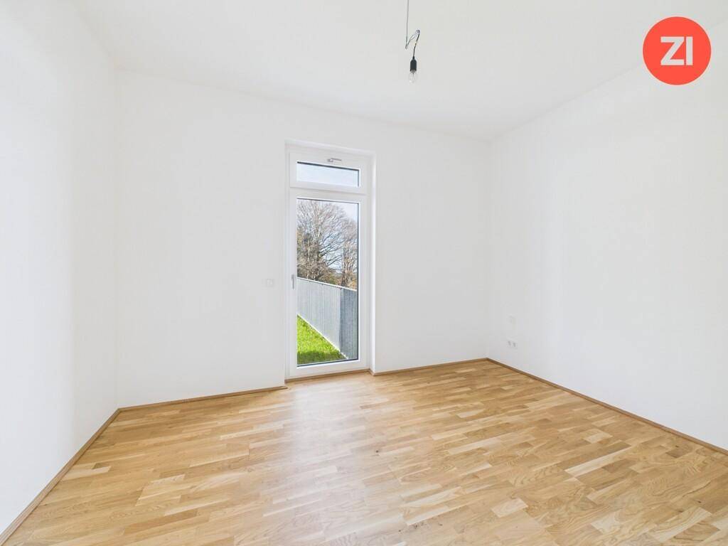 Leeres Zimmer mit Parkettboden und einem Fenster, das viel Tageslicht hereinlässt.