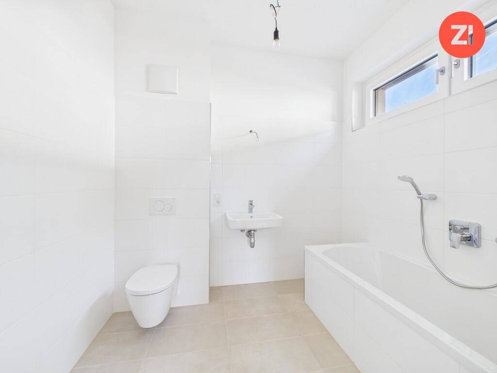 Modernes Badezimmer mit Badewanne, WC und Waschbecken in hellen Fliesen und Fenster.