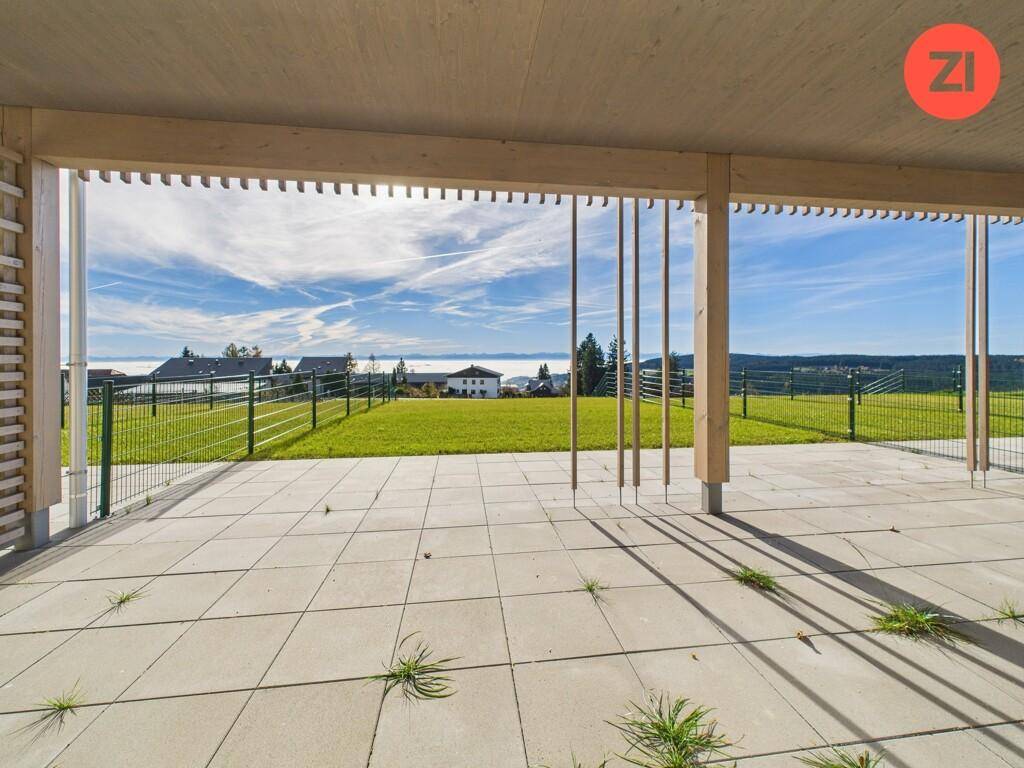 Große gepflasterte Terrasse mit Holzpergola und weitem Blick über grüne Felder.