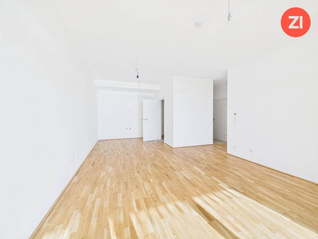 Geräumiger, unmöblierter Raum mit hellem Holzboden und weiß gestrichenen Wänden.