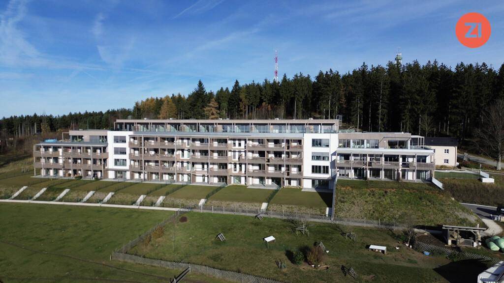 Weitläufige Luftaufnahme eines modernen Wohnkomplexes, eingebettet in grüne Natur und Waldrand.