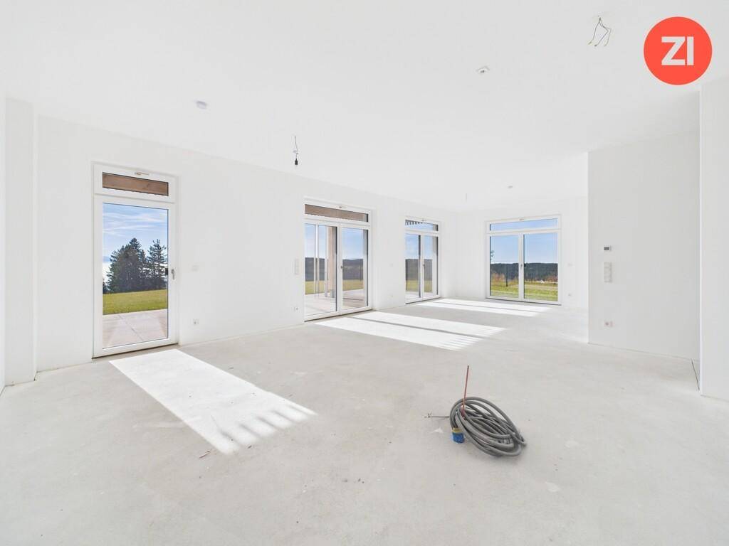 Lichtdurchfluteter Wohnraum im Rohbau mit mehreren Fenstertüren und Blick ins Grüne.