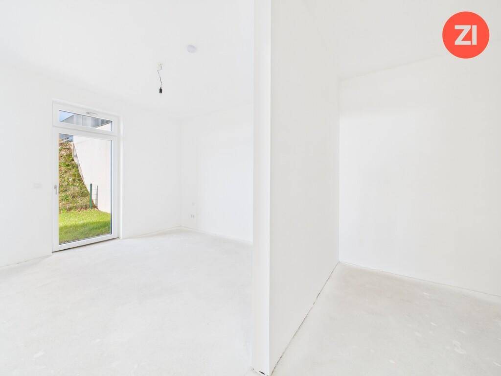 Heller Raum im Rohbau mit Fenster und Zugang zum Außenbereich, noch ohne Bodenbelag.