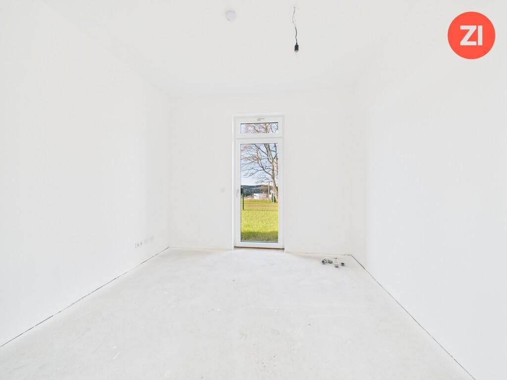 Unmöbliertes Zimmer im Neubau mit großem Fenster und Blick auf die grüne Umgebung.