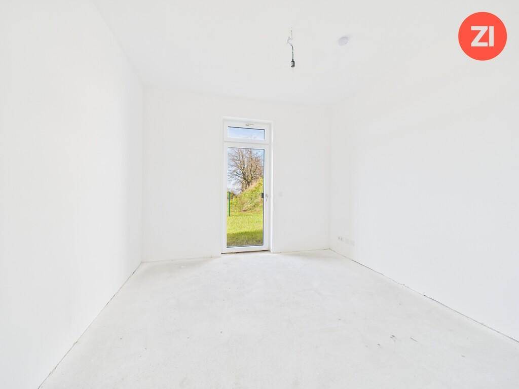 Leeres Zimmer im Neubau mit einem hohen Fenster, das viel Tageslicht hereinlässt.