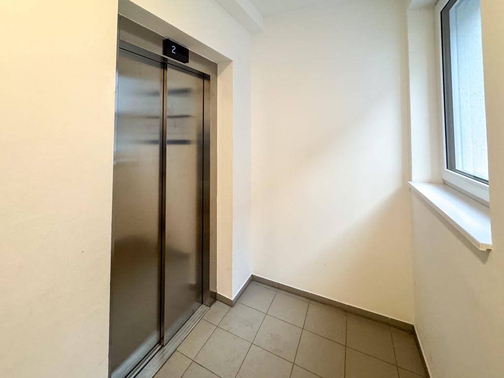 Moderner Aufzug in einem hellen Flur mit Fliesenboden und Fenster.
